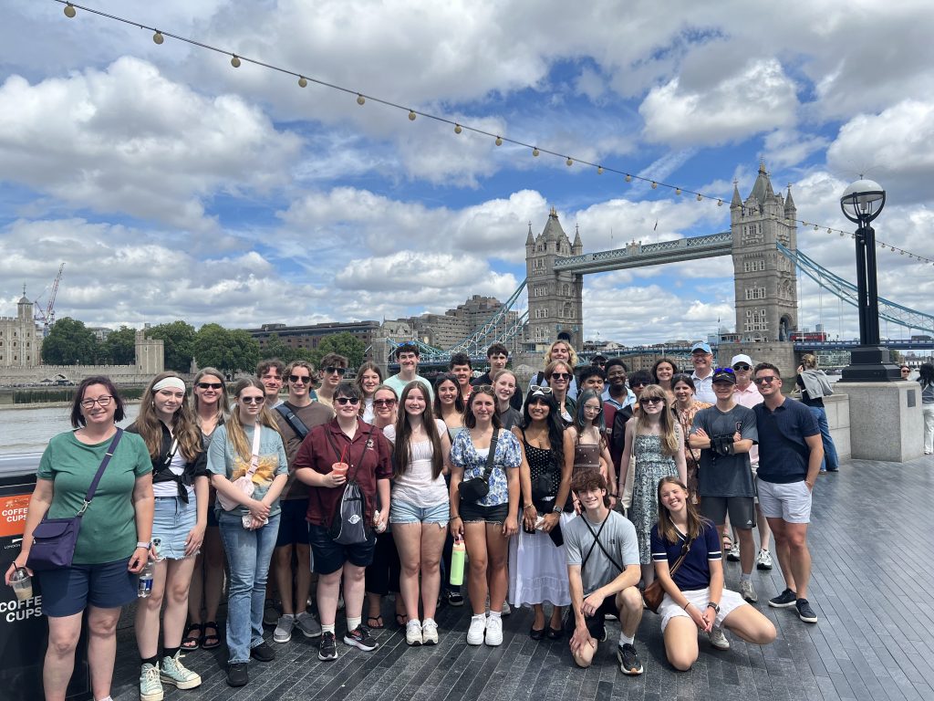 group of travelers smiling and posing for picture in front of large bridge